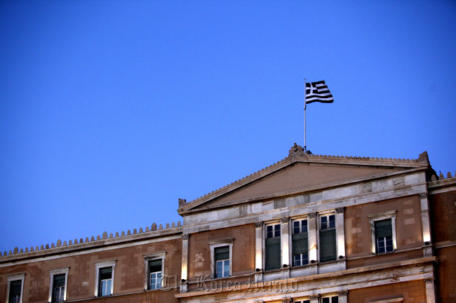 A Greek national flag flies above the parliament building in Athens. Bloomberg