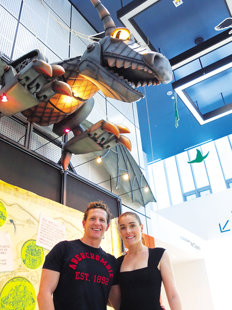 The Australian stars of “Wicked,” David Harris (left) and Jemma Rix, stand under a copy of the Time Dragon, a set dressing featured in the musical, in the foyer of the Blue Square Music Hall in Itaewon-dong, Seoul, Wednesday. (Maryann Wright/The Korea Herald)