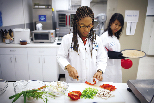 Lockeed Martin research scientist Maya Cooper (left) and Monica Leong prepare a vegan pizza at NASA’s Advanced Food Technology Project at Johnson Space Center on July 3 in Houston. (AP-Yonhap News)