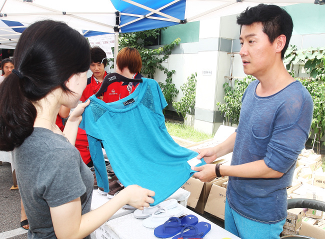 Lee Hyun-woo (right) tries to sell a shirt to a woman at the Social Welfare Society bazaar held in Yeoksam-dong, Seoul, on Wednesday.  Yonhap News