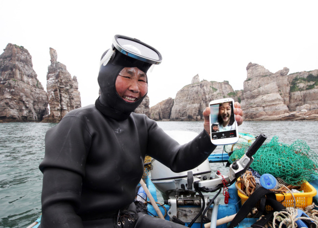 <YONHAP PHOTO-0562> SK 백령도 해상서 HD 보이스 시연 (서울=연합뉴스) 지난 27일 서해 최북단 백령도 두무진 앞 해상에서 김호순(64.해녀)씨가 SK텔레콤의 LTE 기반 고품질 영상통화인 HD Voice를 시연하고 있다. SK텔레콤측은 육지와 멀리 떨어져 전파 환경이 불안정한 도서 지역에서는 처음으로 이루어진 HD Voice 시연을 통해, 읍면 단위 전국망을 넘어 도서 지역까지 완벽한 LTE 전국망이 구축됐다고 밝혔다. 2012.7.29 << SK텔레콤 >> photo@yna.co.kr/2012-07-29 10:35:32/ <저작권자 ⓒ 1980-2012 ㈜연합뉴스. 무단 전재 재배포 금지.>
A traditional sea diver, or haenyeo, places a HD Voice call off the coast of Baengnyeongdo on Friday.  SKT