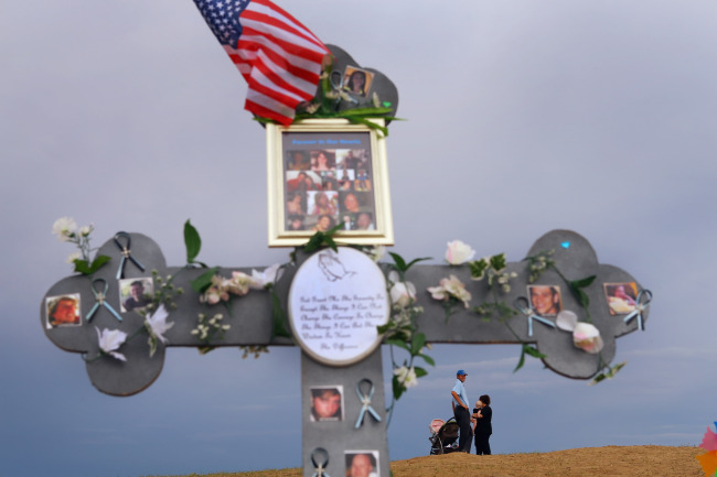 People are seen near a cross adorned with photographs of victims of the mass shooting at the Century 16 movie theater 30 in Aurora, Colorado on July.  AFP-Yonhap News