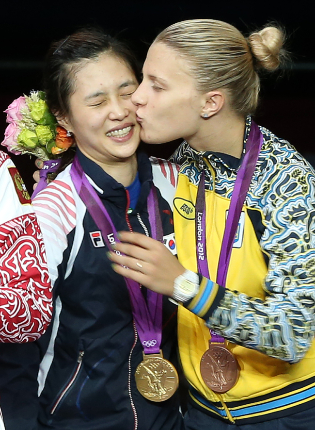 South Korean fencer Kim Ji-yeon (left) receives a kiss from Ukraine’s bronze medalist Olga Kharlan after winning Korea’s first fencing gold medal in the women’s sabre individual event at the 2012 London Olympics on Wednesday. Ahn Hoon/The Korea Herald