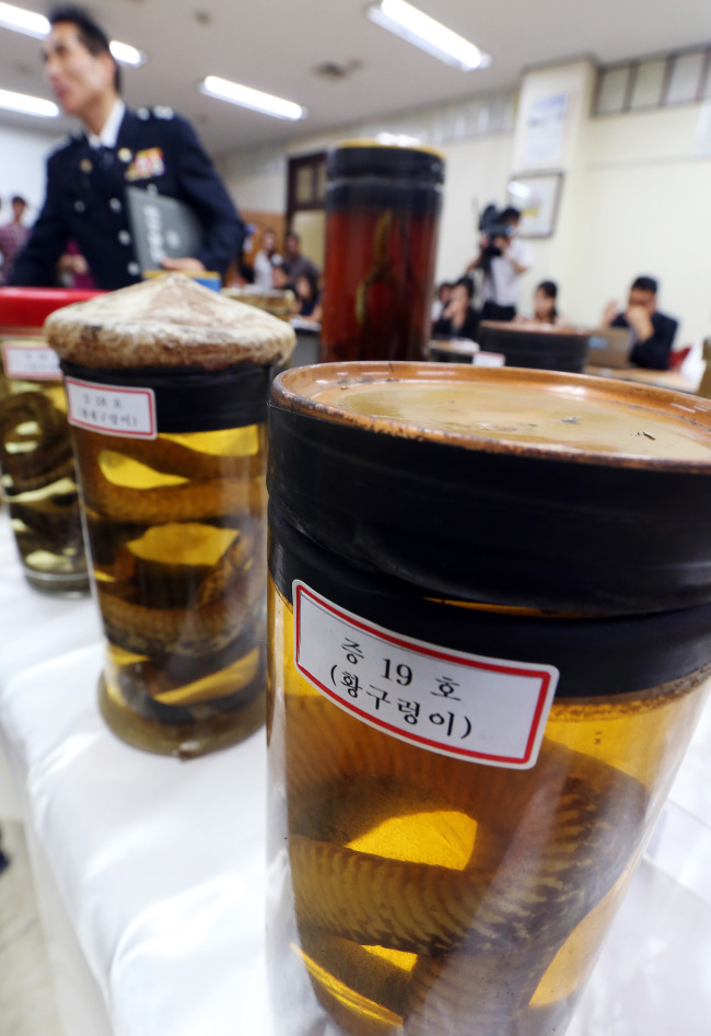 <YONHAP PHOTO-1240> '신월동 출몰 뱀' 건강원에서 탈출 (서울=연합뉴스) 신준희 기자 = 지난 한달여간 서울 양천구 신월동에서 출몰한 뱀들이 인근 건강원에서 나온 것으로 밝혀졌다. 양천경찰서는 지난 5월 경남 밀양 지리산 자락에서 황구렁이와 황새구렁이 등 멸종위기 야생동물을 불법 포획해 뱀탕을 만들 목적으로 보관한 혐의로 건강원 업주 정모(51)씨를 불구속 입건했다고 2일 밝혔다. 정씨는 뱀을 보관하던 망에 구멍이 나 23마리 모두가 도망쳤다고 경찰에 자백했다. 이날 오전 이 사건 관련 브리핑 중인 양천서 회의실에 정씨로부터 압수한 뱀술들이 놓여있다. 2012.8.2 hama@yna.co.kr/2012-08-02 14:04:48/ <저작권자 ⓒ 1980-2012 ㈜연합뉴스. 무단 전재 재배포 금지.>
A police officer points at alcoholic beverages containing endangered snakes confiscated from a traditional health-supplement shop in Sinwol-dong in southwestern Seoul on Thursday.  Yonhap News
