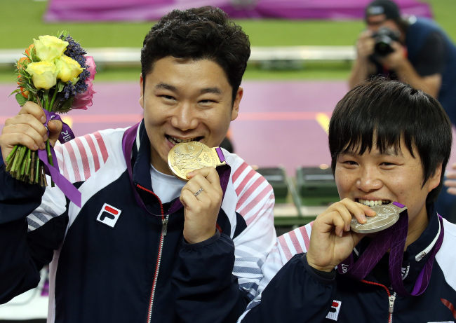 South Korea's Jin Jong-oh (left) and Cho Young-rae bite their gold and silver medals as they leave the firing range following the victory ceremony in the men’s 50-meter pistol shooting at the 2012 Summer Olympics, Wednesday, Aug. 5, 2012, in London. (London Olympic Joint Press Corps)
