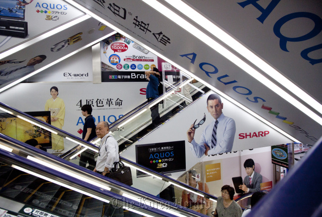 Shoppers ride on escalators past Sharp Corp. advertisements at an electronics store in Tokyo.  Bloomberg