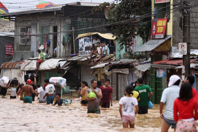 Residents on a rooftop watch others wade along a flooded road in Marikina, east of Manila.  AP-Yonhap News