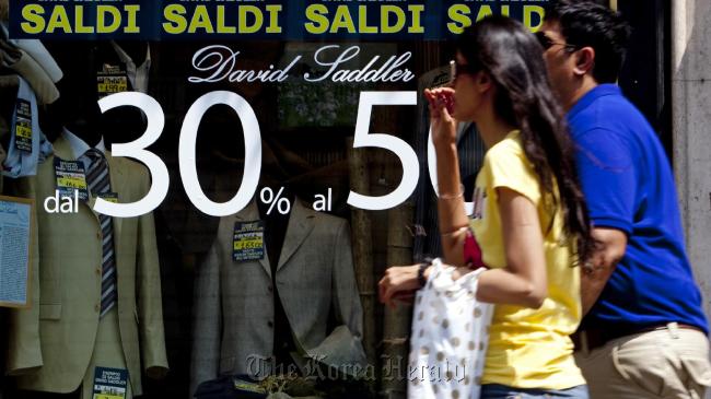 Pedestrians carry shopping bags past a store advertising a sale in its window display in Rome.   Bloomberg