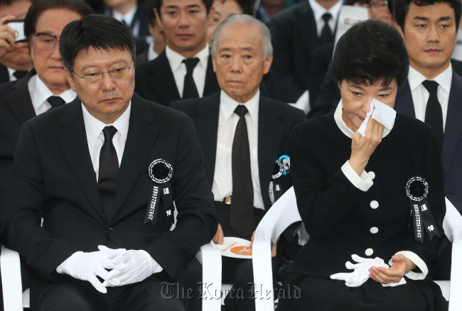 Former Saenuri Party chairwoman Park Geun-hye dabs her face with a handkerchief as she sits next to her brother Ji-man while attending the 38th memorial service for her late mother and former first lady Yuk Young-soo at Seoul National Cemetery in Dongjak-dong, Seoul, Wednesday.   Yonhap News