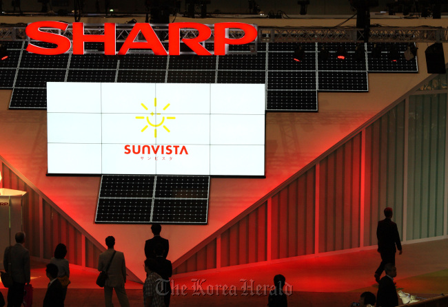 Visitors walk in front of a display of solar panels in the Sharp Corp. booth at CEATEC JAPAN at Makuhari Messe in Chiba City, Japan.   Bloomberg