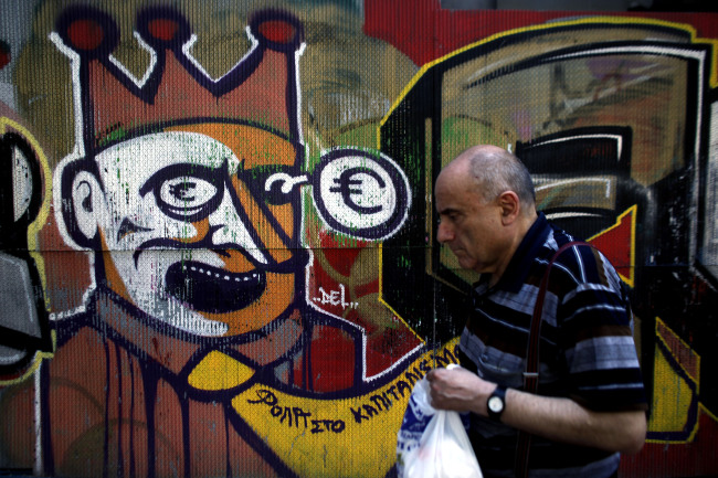 A pedestrian walks past euro-crisis graffiti painted on a wall in Athens.    Bloomberg