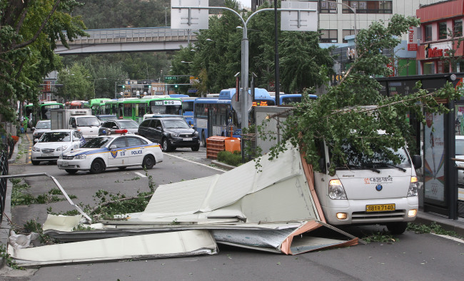 A truck is hit by storm debris from a nearby building and a broken tree on a road in Seoul on Tuesday.   Yonhap News