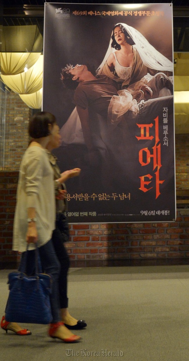People pass by a poster of Kim Ki-duk’s film “Pieta” displayed at Cinecube in Gwanghwamun on Monday.   Kim Myung-sub/The Korea Herald