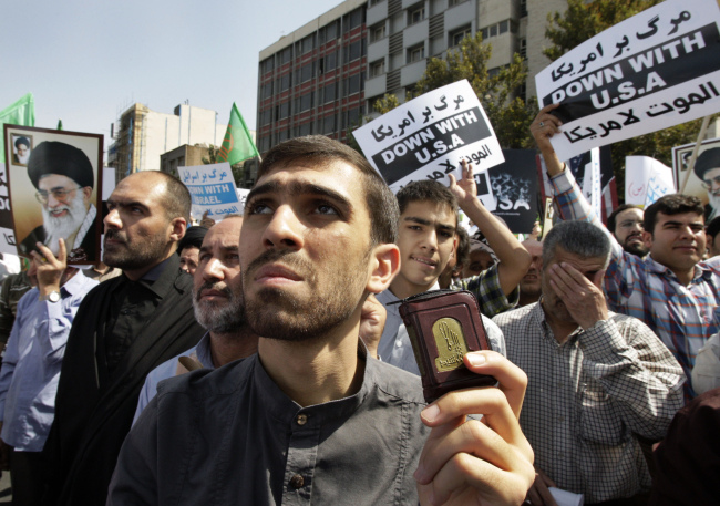 An Iranian worshipper holds a copy of the Quran, Muslims’ holy book, as the others hold up anti-U.S. and anti-Israel placards and posters showing Iranian supreme leader Ayatollah Ali Khamenei, and late revolutionary founder Ayatollah Khomeini, during a protest after their Friday prayers, as part of widespread anger across the Muslim world about a film ridiculing Islam’s Prophet Muhammad.   AP-Yonhap News