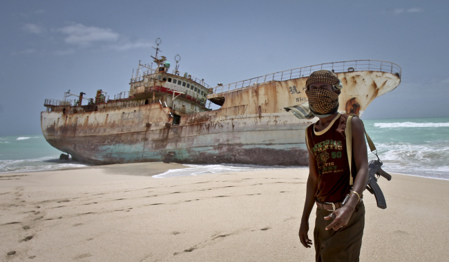 In this photo taken Sunday, masked Somali pirate Abdi Ali stands near a Taiwanese fishing vessel that washed up on shore after the pirates were paid a ransom and released the crew, in the once-bustling pirate den of Hobyo, Somalia.   AP-Yonhap News
