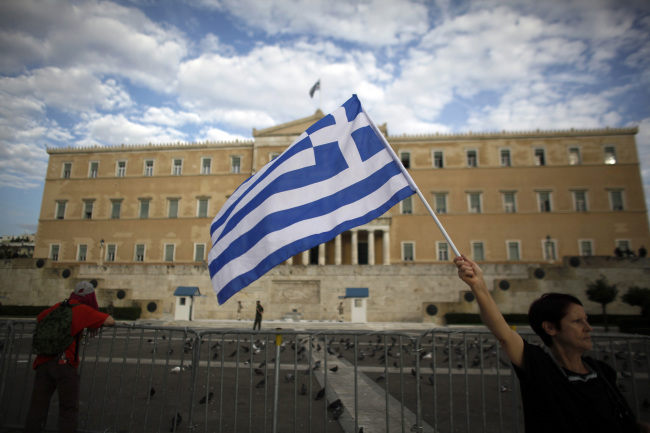 A demonstrator waves a Greek national flag ahead of a protest against tomorrow's visit by Angela Merkel, Germany's chancellor, opposite the Greek parliament building in Athens, Greece, on Monday, Oct. 8, 2012. Greece's need for bailouts and the German-led conditions attached to the emergency loans have made Merkel the face of austerity to Greeks. Photographer: Kostas Tsironis/Bloomberg
A demonstrator waves a Greek national flag ahead of a protest against a visit by Angela Merkel, Germany’s
chancellor, opposite the Greek parliament building in Athens on Oct. 9.   Bloomberg