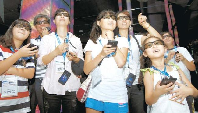 Wearing 3-D glasses, family members of an SK Hynix employee try stereoscopy at T.um, the company’s IT exhibition
booth. (SK Hynix)