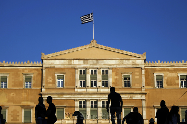 Pedestrians stand in front of the Greek parliament building as the country’s national flag flies from the top in Athens.   Bloomberg