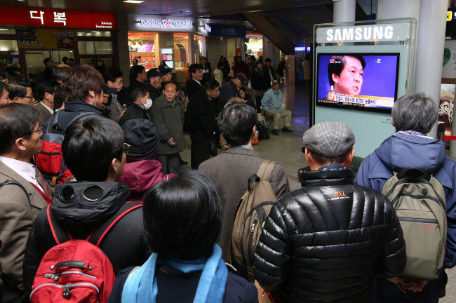 People at Seoul Station watch television broadcast of Ahn Cheol-soo’s announcement that he was withdrawing from the presidential race Friday. (Yonhap News)
