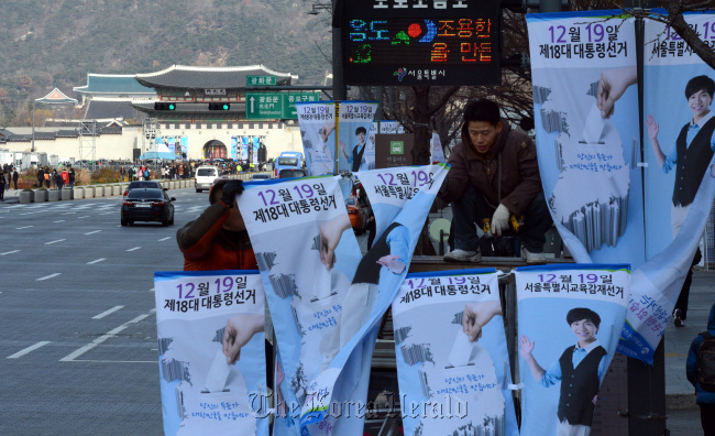 Government workers put up banners for the Dec. 19 presidential election and the election for the superintendent of the Seoul Metropolitan Office of Education near Gwanghwamun Square in Seoul on Sunday.   Chung Hee-cho/The Korea Herald