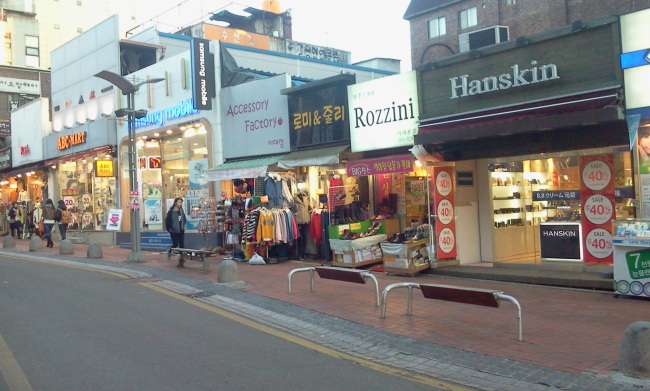 An emptied shopping alley near Ewha Womans University in western Seoul showing shuttered clothing boutiques with racks pulled inside a snapshot of the Ewha shopping district during its early 2010s decline
