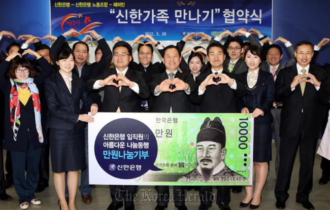 Shinhan Bank president Seo Jin-won (front row, center) and Happy Bean Foundation chairman Kwon Hyuk-il (front row, third from right) pose with other Shinhan employees in March after signing the contract for the 10,000 won donation project in central Seoul.   Shinhan Bank
Shinhan Bank president Seo Jin-won (front row, center) and Happy Bean Foundation chairman Kwon Hyuk-il (front row, third from right) pose with other Shinhan employees in March after signing the contract for the 10,000 won donation project in central Seoul.   Shinhan Bank