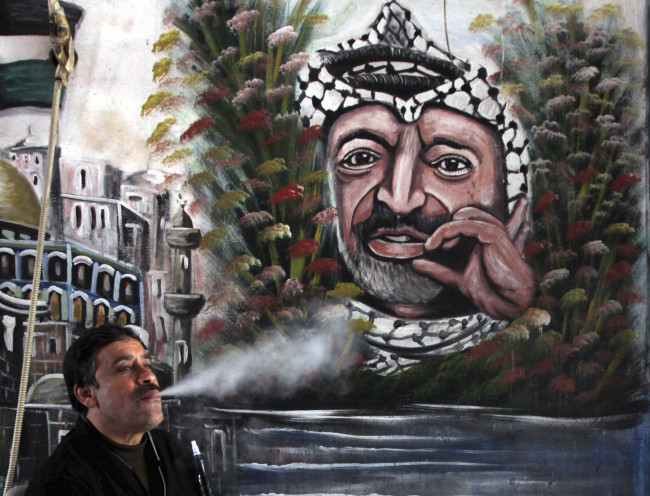 A Palestinian man smokes a water pipe next to a mural of late Palestinian leader Yasser Arafat, in the West Bank town of Jenin, Tuesday.   AP-Yonhap News