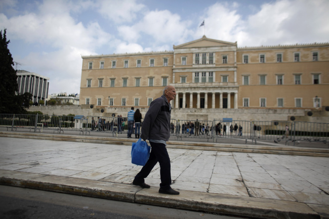 A pedestrian carries his shopping bag past the Greek parliament on Syntagma square in Athens.   Bloomberg