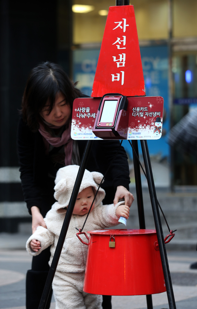 A baby puts money into the Salvation Army kettle on a Myeong-dong street in Seoul. A credit card reader is installed above the kettle to take donations  by card for the first time from this year.   Yonhap News