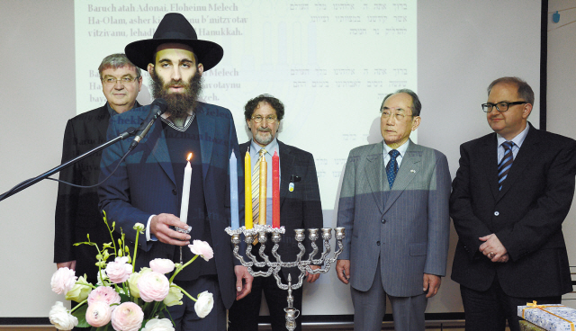 Rabbi Osher Litzman (second from left) of Chabad Jewish Community of Korea prepares to light the menorah candles
on the fourth day of Hanukkah as Israeli Ambassador to Korea Tuvia Israeli (left) looks on at the Israeli Culture
Center in southern Seoul, Tuesday. Ahn Hoon/The Korea Herald