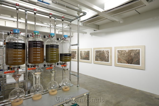Photos of the autumn landscape at Mt. Seorak taken by artist Baek Jung-ki (right) are on display at SongEun ArtSpace. On the left is the equipment the artist made to grind autumn leaves and extract the ink used to print the photos.   SongEun Art and Cultural Foundation