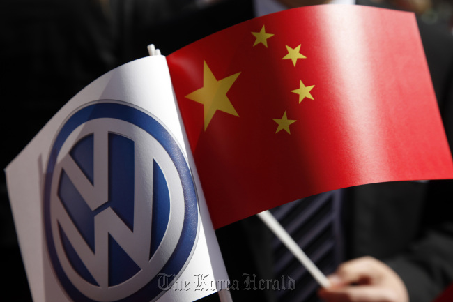 A man holds a Volkswagen AG flag (left) alongside the Chinese national flag during the German-Chinese signing ceremony at Volkswagen AG’s headquarters.    Bloomberg