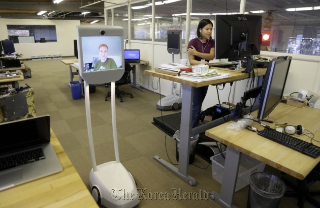 Senior software enginee Josh Faust, seen on screen, navigates his company’s office using a Beam remote presence system, as fellow engineer Stephanie Lee (right) works on a project at Suitable Technologies in Palo Alto, California.   AP