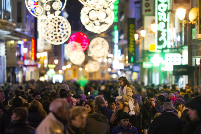 Christmas lights illuminate shoppers in a crowded shopping street in central Madrid on Saturday.   Bloomberg