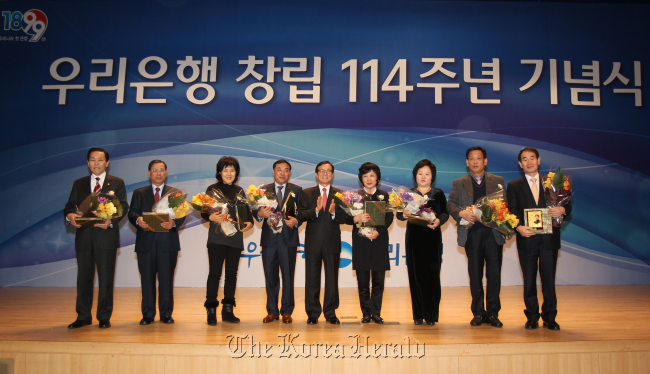 Woori Bank president & CEO Lee Soon-woo (center) poses with customers during an event to celebrate the 114th anniversary of the financial firm’s foundation at its headquarters in downtown Seoul on Friday. Its former entity was Daehan Cheonil Bank, established in 1899 with funds from then-Korean Emperor Gojong.   Woori Bank
