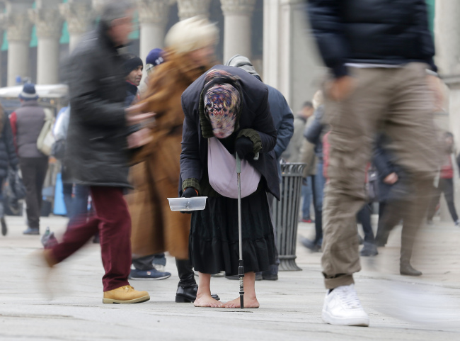 A woman begs for money amid passersby in downtown Milan on Tuesday.   AP-Yonhap News