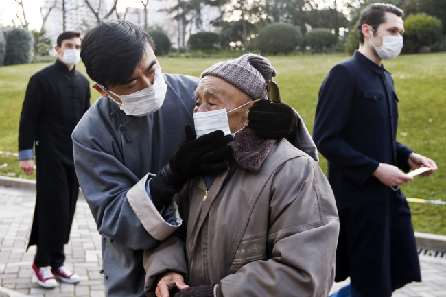 A man helps an elderly passer-by put on a mask while others hand out free masks to pedestrians in an effort to promote public awareness to use masks for protection from polluted air in Shanghai on Friday.   AP-Yonhap News