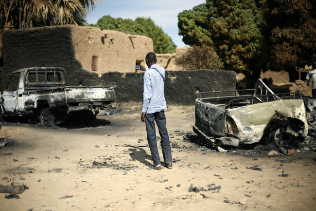 An unidentified man takes a picture of the charred remains of trucks used by radical Islamists on the outskirt of Diabaly, Mali, Monday.   AP-Yonhap News