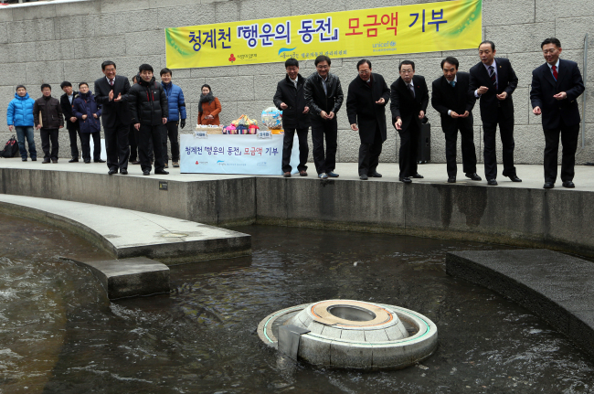 Officials from the Korean Committee for UNICEF, a committee to manage palseokdam coins, Seoul Metropolitan Facilities Management Corp. and Community Chest of Korea throw coins into palseokdam during a coin donation ceremony in Seoul on Tuesday.   Yonhap News