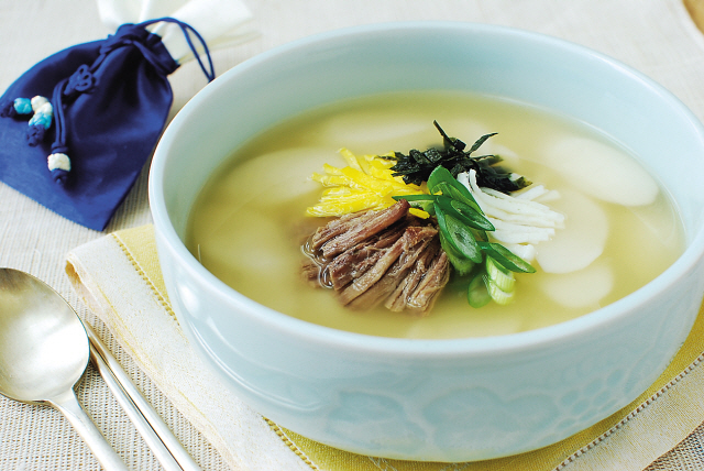 Traditional Korean tteokguk served in a white bowl with sliced rice cakes floating in clear beef broth, garnished with egg, scallion and gim for Lunar New Year