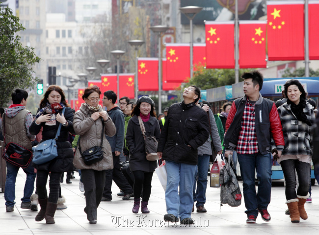 Chinese flags hang on lamp posts as pedestrians walk through the East Nanjing Road shopping area of Shanghai.   Bloomberg