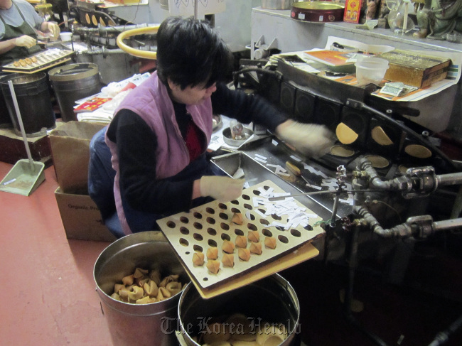 A woman deftly folds and inserts fortunes into cooling cookies at the Golden Gate Fortune Cookie Company, which produces 20,000 handmade fortune cookies a day in San Francisco’s Chinatown.   Chicago Tribune/MCT