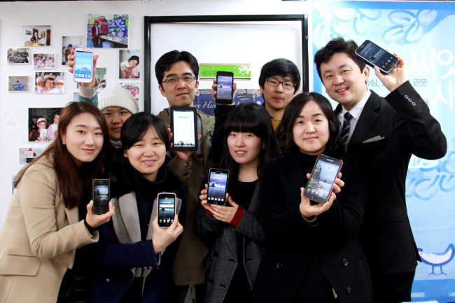 Park Ki-tae (right, back row), founder and leader of VANK, and its members hold their smartphones after changing their wallpapers into Dokdo photos.   Yonhap News
