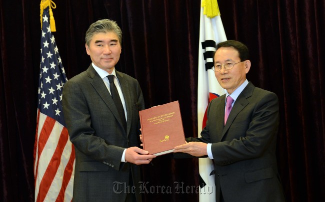 United States Ambassador to Korea Sung Kim (left) and Min Byoung-chul, founder and chair of the nonprofit Sunfull Movement, hold up a book of condolence messages at the U.S. Embassy in Korea, Tuesday, that Min presented to Kim for victims of the Sandy Hook Elementary School shooting, their families and the people of Newtown, Connecticut, in the U.S.   Park Hae-mook/The Korea Herald