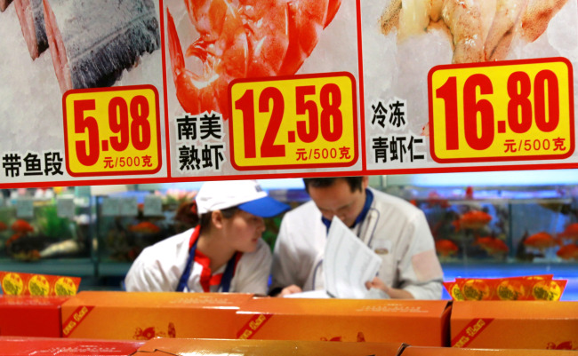 Staff members check goods behind price tags at a supermarket in Shanghai on Saturday.   Xinhua-Yonhap News