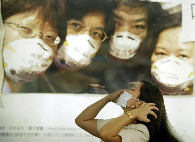 In a file picture taken in April 2003, a woman puts on a mask under a poster urging people in Hong Kong to wear them to protect against a killer outbreak of pneumonia known as SARS.   AFP-Yonhap News