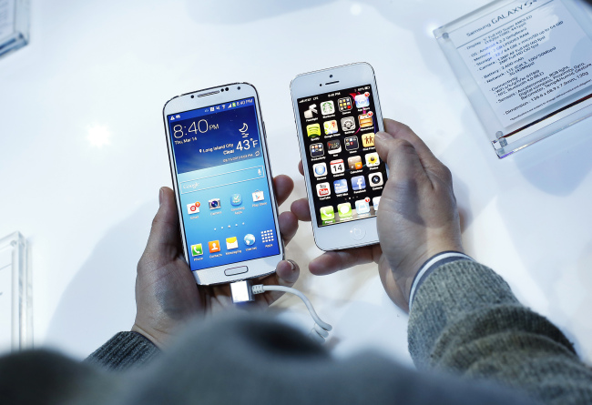 An attendee holds a Samsung Electronics Co. Galaxy S4 smartphone (left), next to Apple’s iPhone 5 during an event at Radio City Music Hall in New York in March. Samsung unveiled the Galaxy S4 with a bigger screen and software that tracks eye movements.   Bloomberg