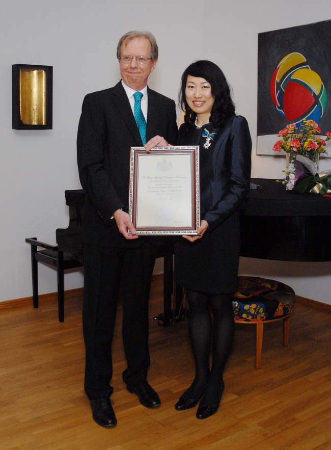 Swedish Ambassador Lars Danielsson (left) and local Korean staffer Bak Hyun-jung hold up a certificate accompanying the Royal Order of the Polar Star she received during a ceremony at the ambassador’s residence in the Seongbuk-dong neighborhood of Seoul, Monday.   Swedish Embassy