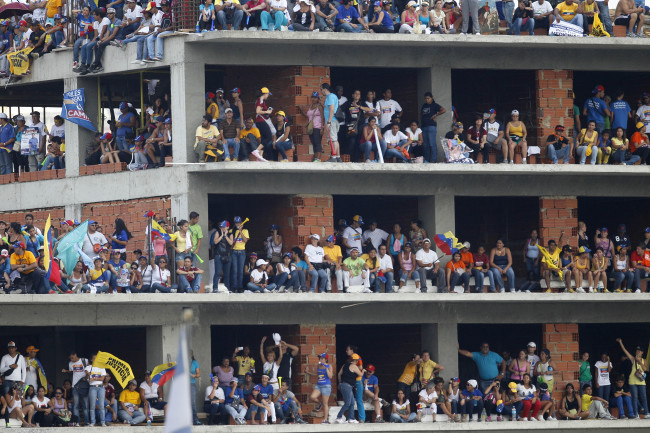 Supporters stand on a building under construction during a campaign rally for opposition presidential candidate Henrique Capriles at Bolivar Avenue in Caracas on Sunday.   AP-Yonhap News