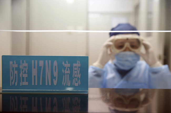 A health worker wearing protective clothing adjusts her goggles at a desk with a sign that reads “H7N9 flu prevention” at a hospital in Shanghai, China, Monday.   AP-Yonhap News